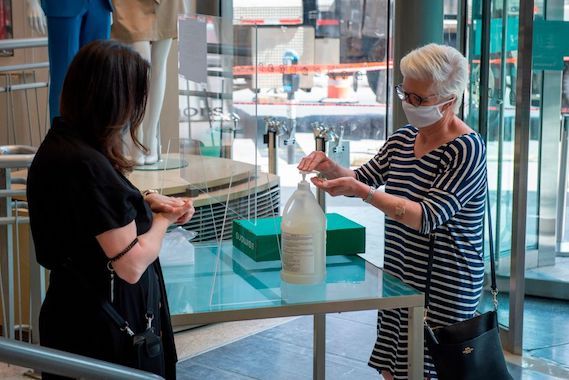 Une dame se met du liquide désinfectant sur les mains à l'entrée d'un magasin.