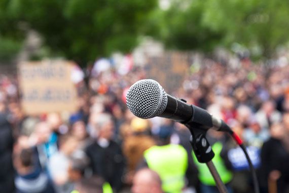 Un micro sur une scène devant des manifestants.