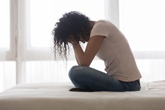 Une femme se tient la tête entre les mains assise sur son lit.