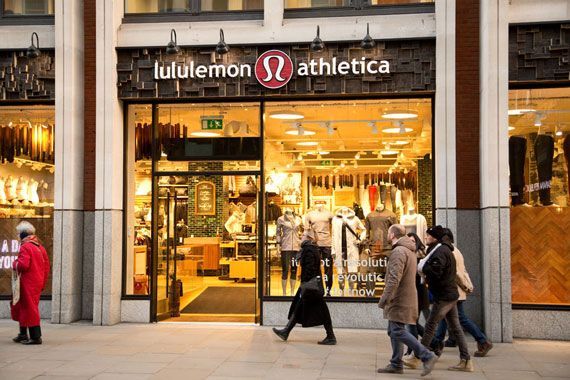 Une devanture de boutique Lululemon devant laquelle des gens marchent.