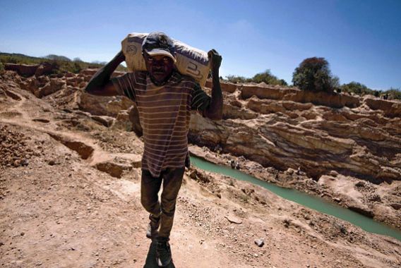 Un homme porte sur son dos un sac rempli de minerais. 