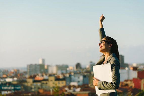 Une femme lève le point vers le ciel en étant heureuse.