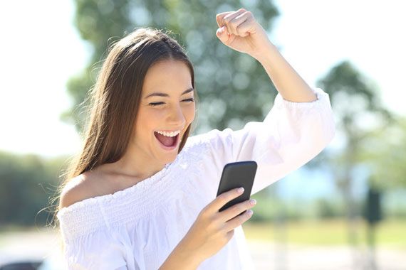 Une femme ayant gagné un pari en ligne et regardant l'écran de son téléphone intelligent.