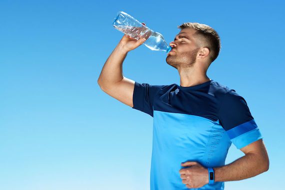 Un homme sportif boit dans une bouteille d'eau.